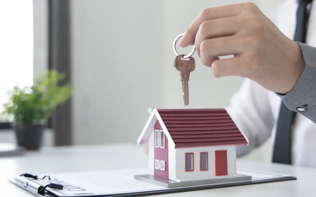 Hand holding house key over miniature house model.