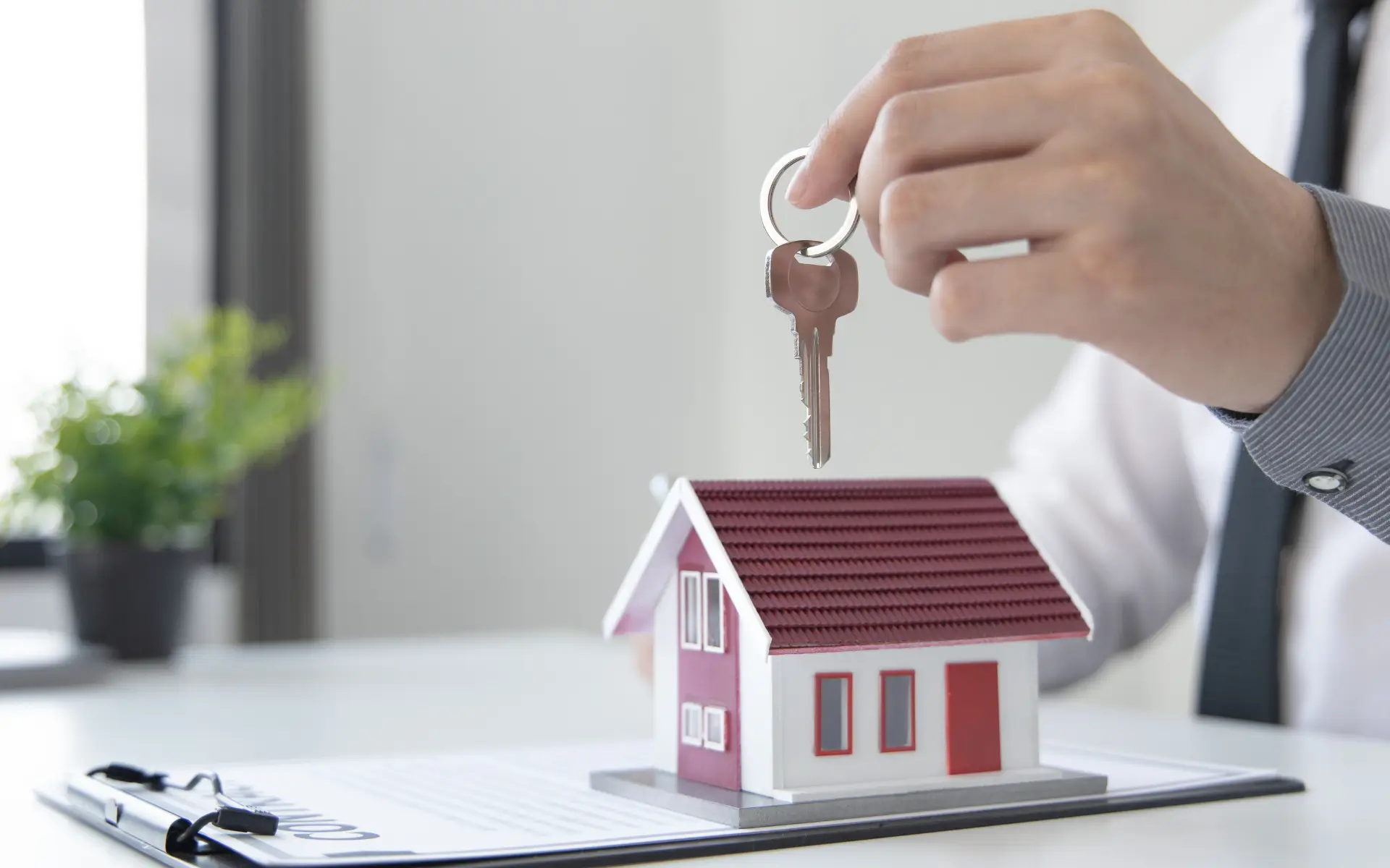 Hand holding house key over miniature house model.