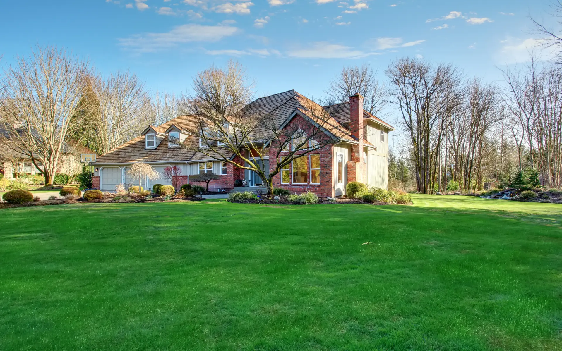 A large, attractive house with a green lawn and trees under a clear blue sky.