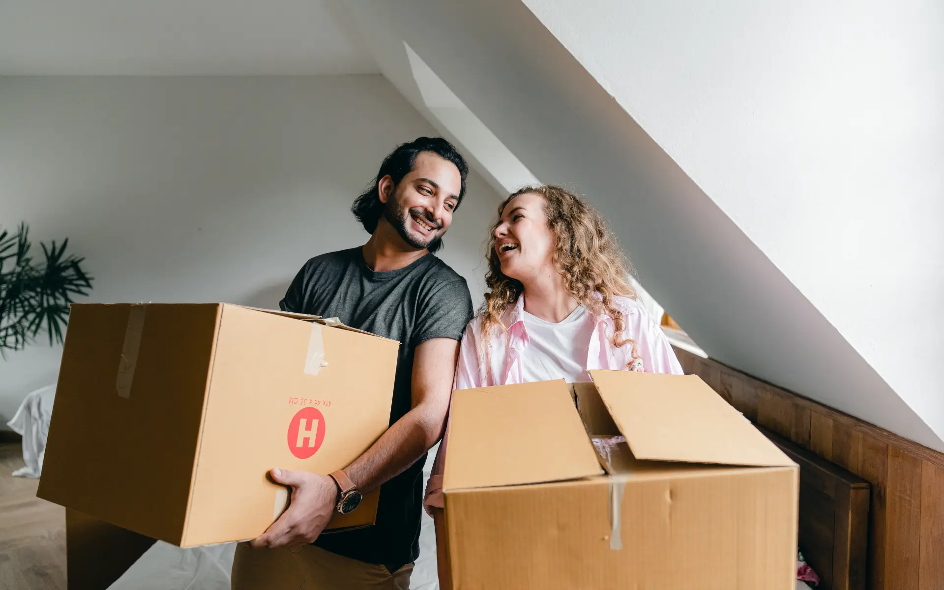 A smiling couple carrying moving boxes in a new home.