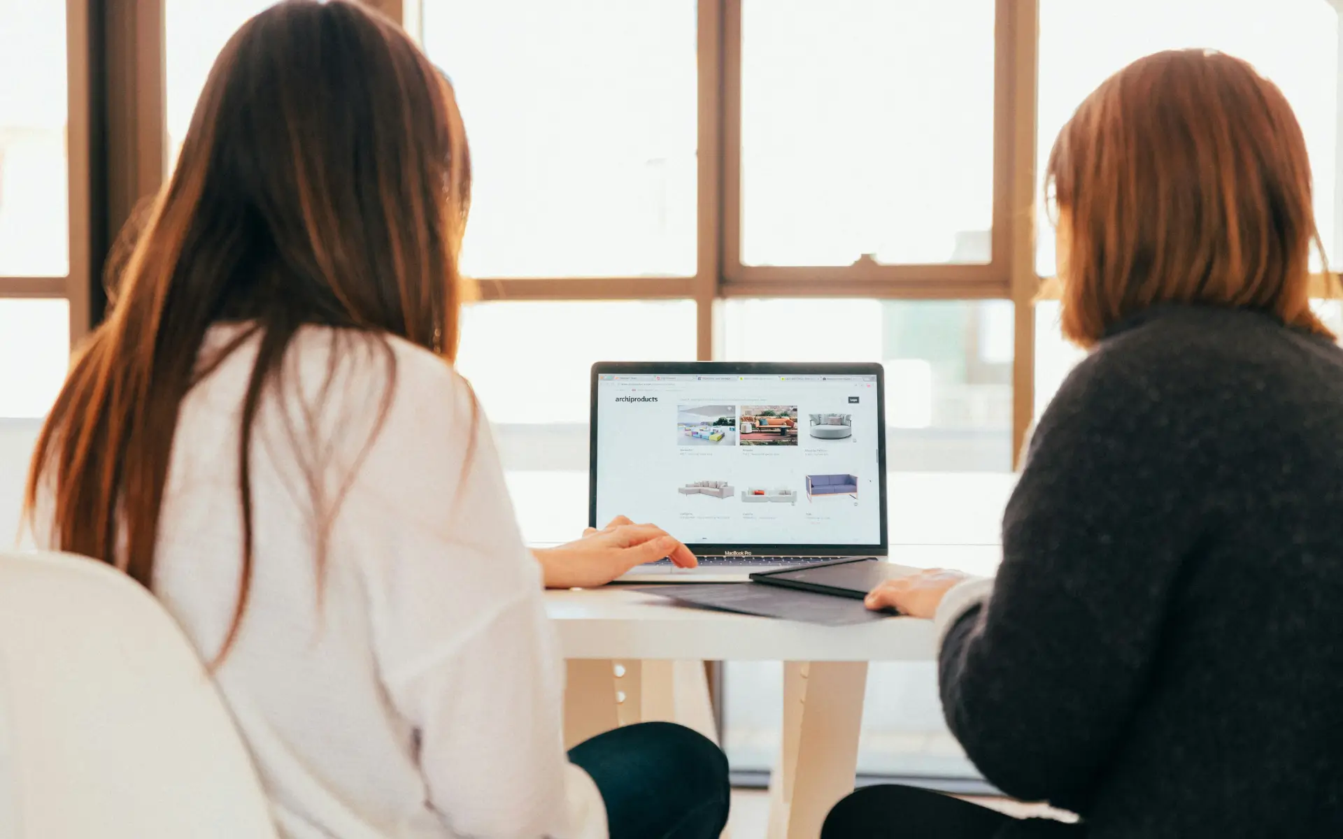 Two people, seen from behind, are collaborating on a laptop.