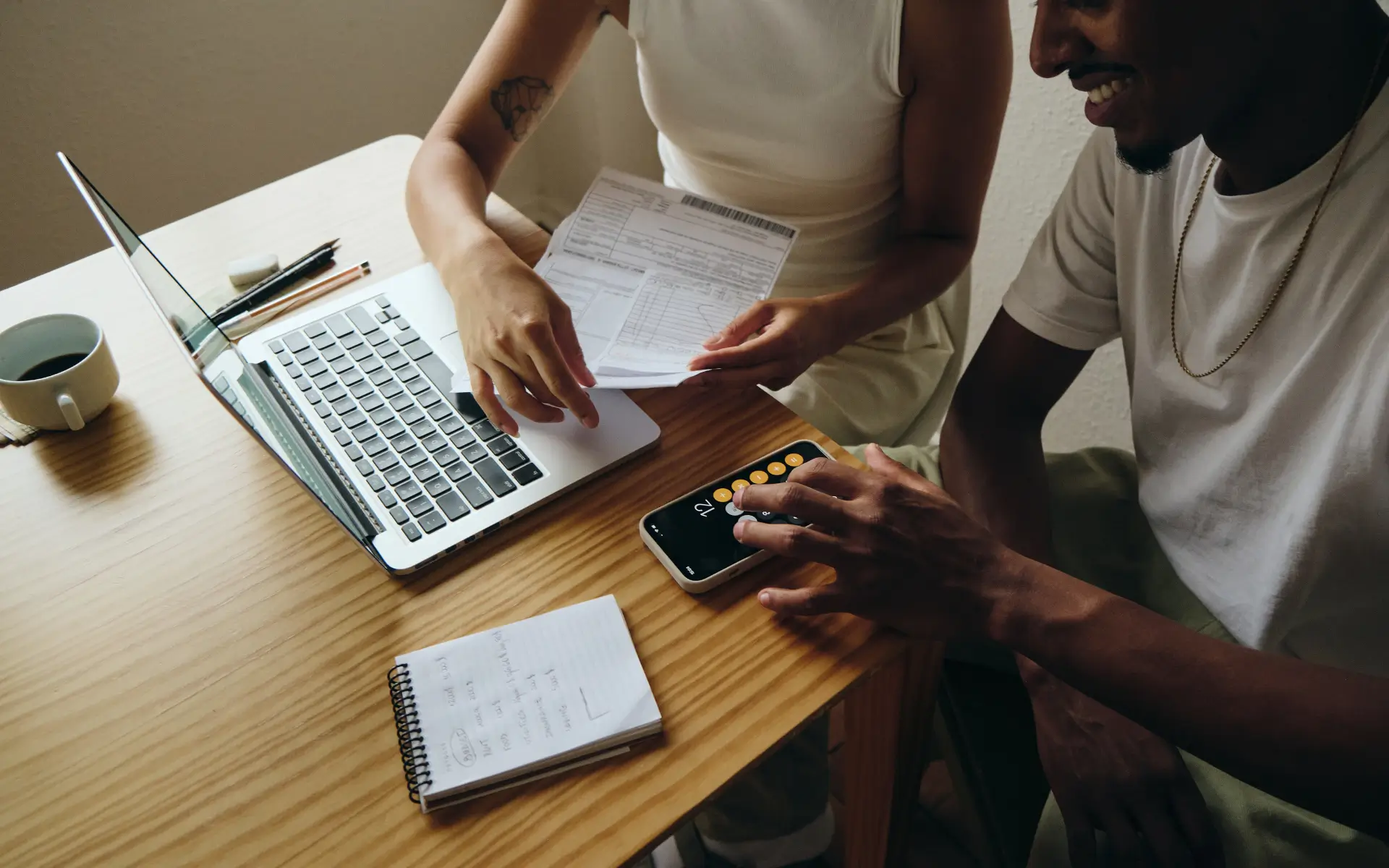Two people reviewing documents and working on a laptop and smartphone at a table.